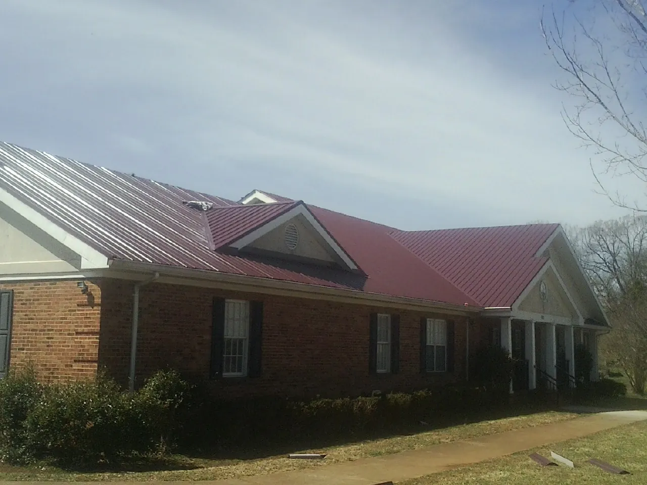 Red metal roof with gabled entries on a long brick building, from a Hail Damage Roof Repair job in Mullan