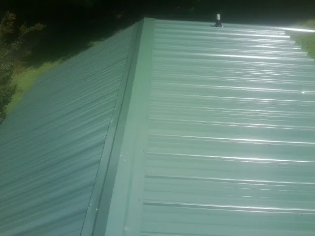 New green metal panels meeting at the ridge of a roof — Flat Roof Repair work by our crew in Mullan
