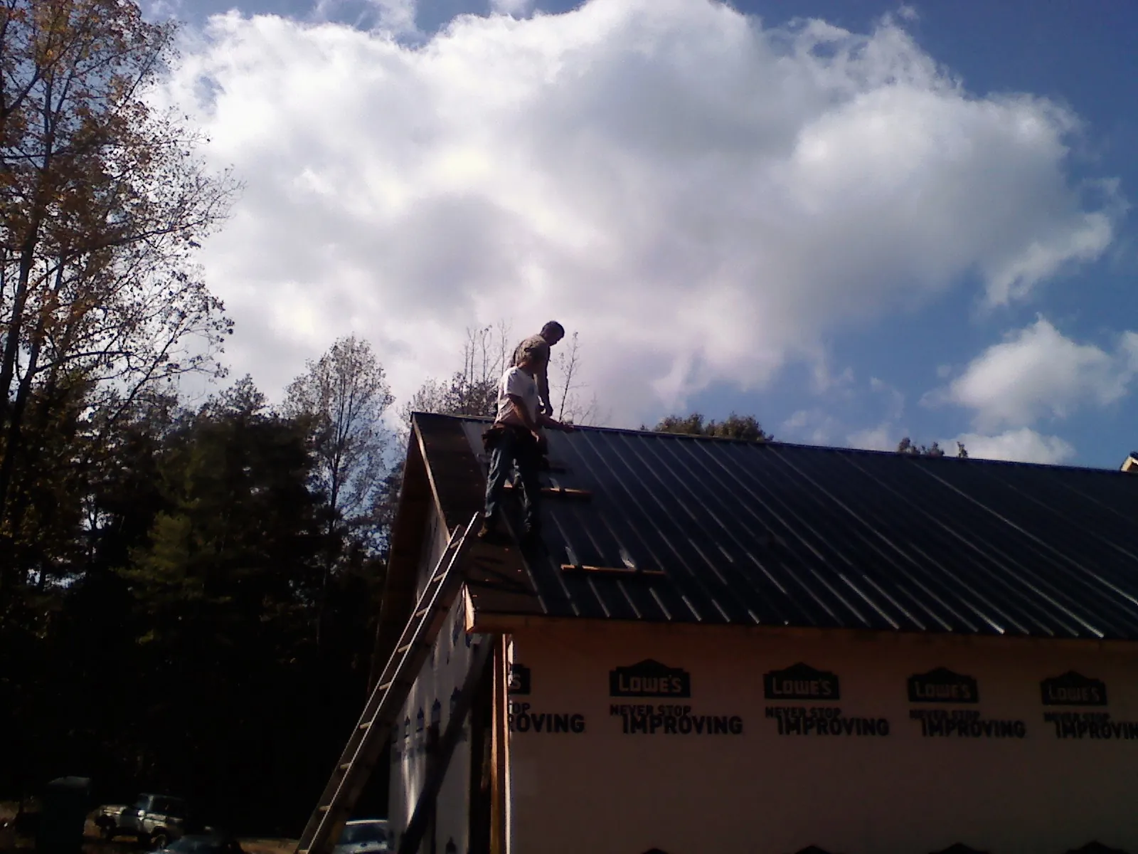Roofer fastening dark metal panels high against a cloudy sky, from a Roof Inspection job in Mullan